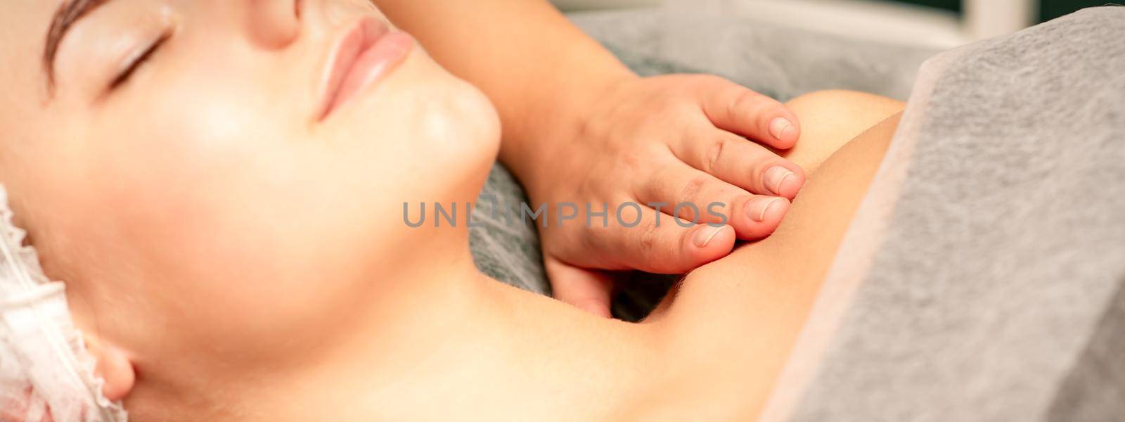 Massaging female breast, and shoulder. Young beautiful caucasian woman with closed eyes receiving chest and shoulders massage in beauty spa salon. by okskukuruza