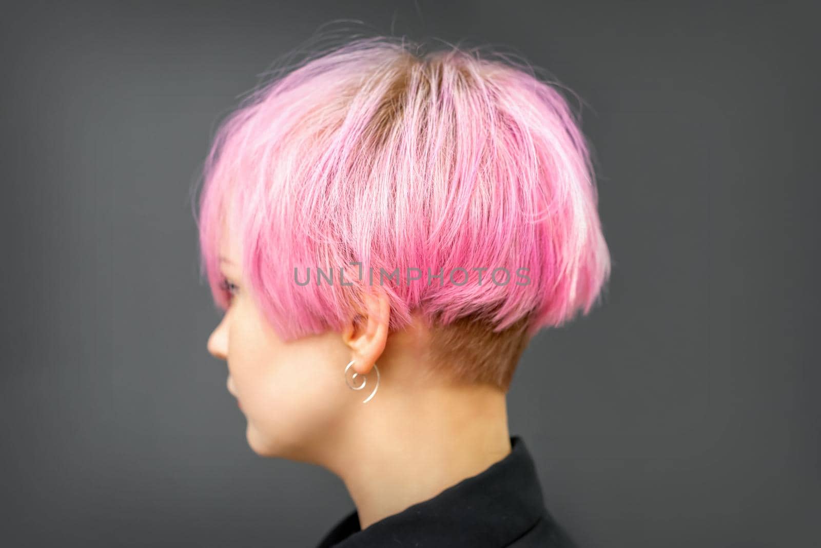 Profile of a beautiful young caucasian woman with short bob pink hairstyle on dark gray background