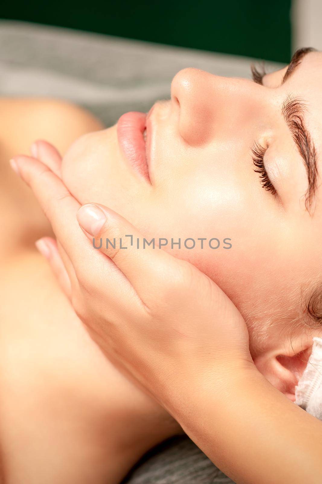 Facial massage. Hands of a masseur massaging neck of a young caucasian woman in a spa salon, the concept of health massage. by okskukuruza