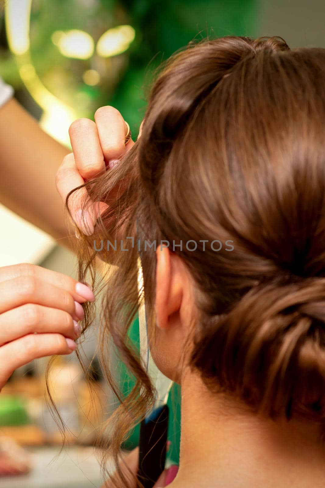 Hairstyling bride. A female hairdresser makes styling hair for the beautiful young caucasian woman in a beauty salon