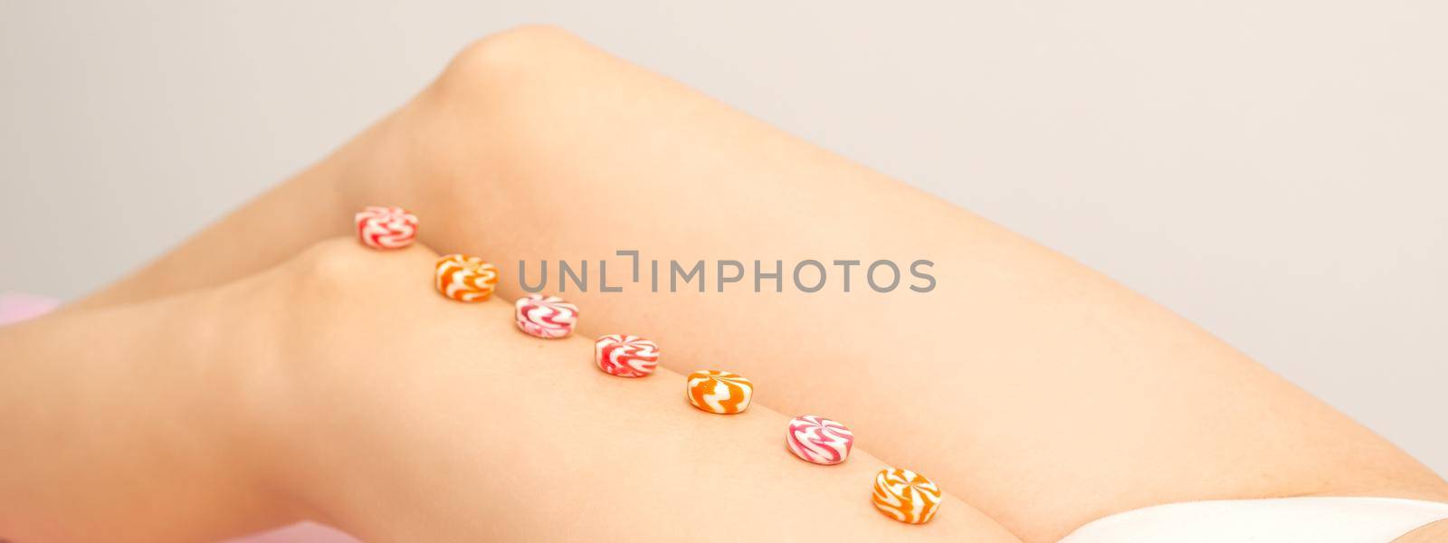 Depilation, waxing concept. Round candies lying down in a row on the female leg, close up. by okskukuruza