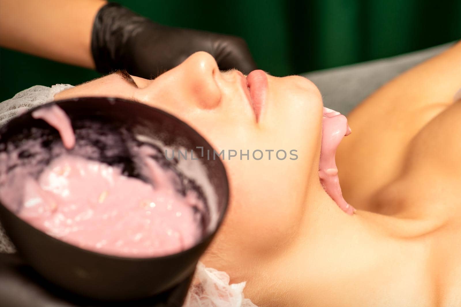 Beautiful young caucasian woman receiving an alginic mask to the face in beauty salon. Facial skin treatment