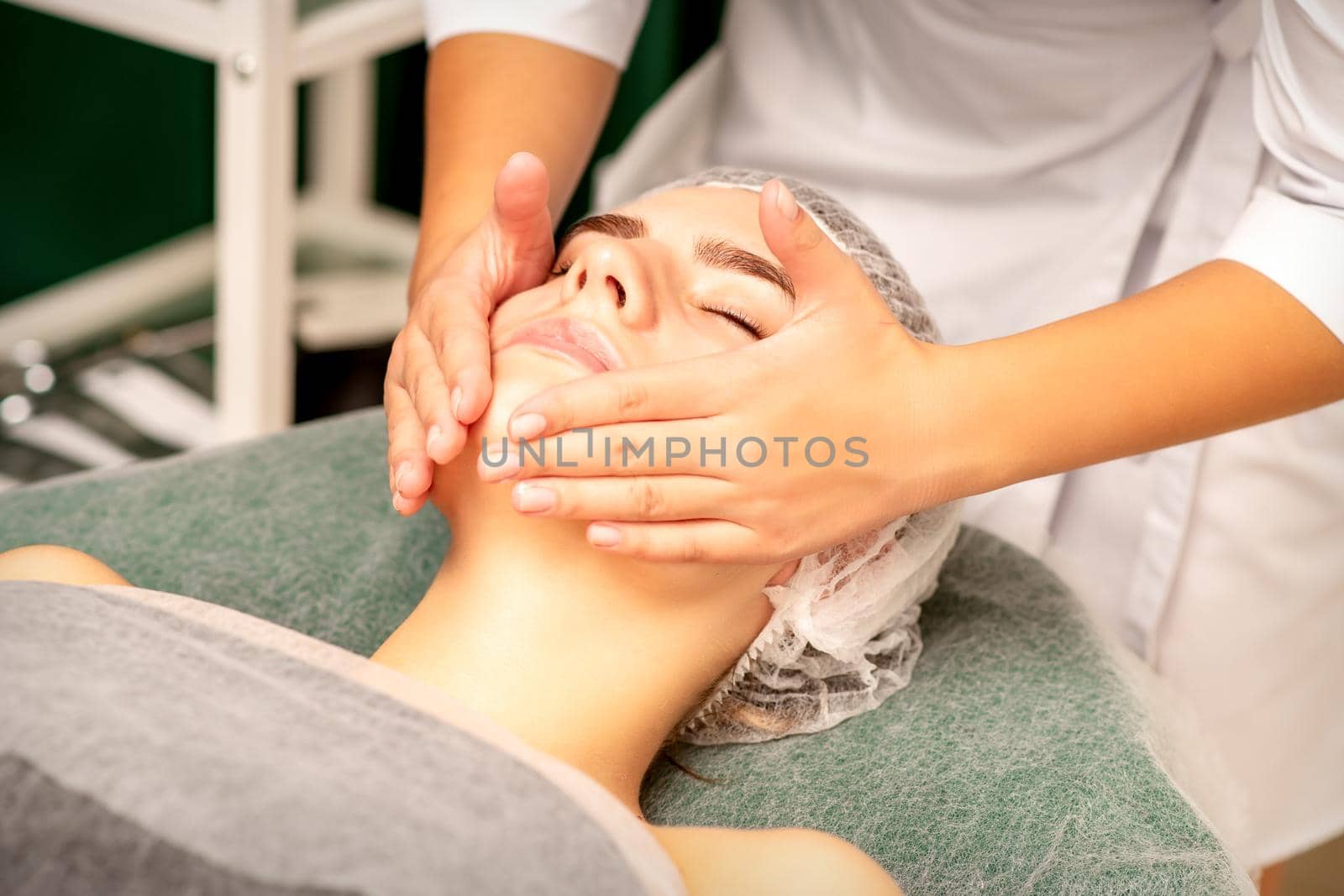 Facial treatment massage. Beautiful young caucasian woman with perfect skin receiving face and neck massage at a beauty spa. by okskukuruza