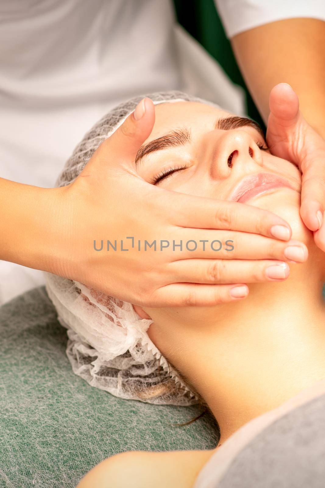 Facial treatment massage. Beautiful young caucasian woman with perfect skin receiving face and neck massage at a beauty spa