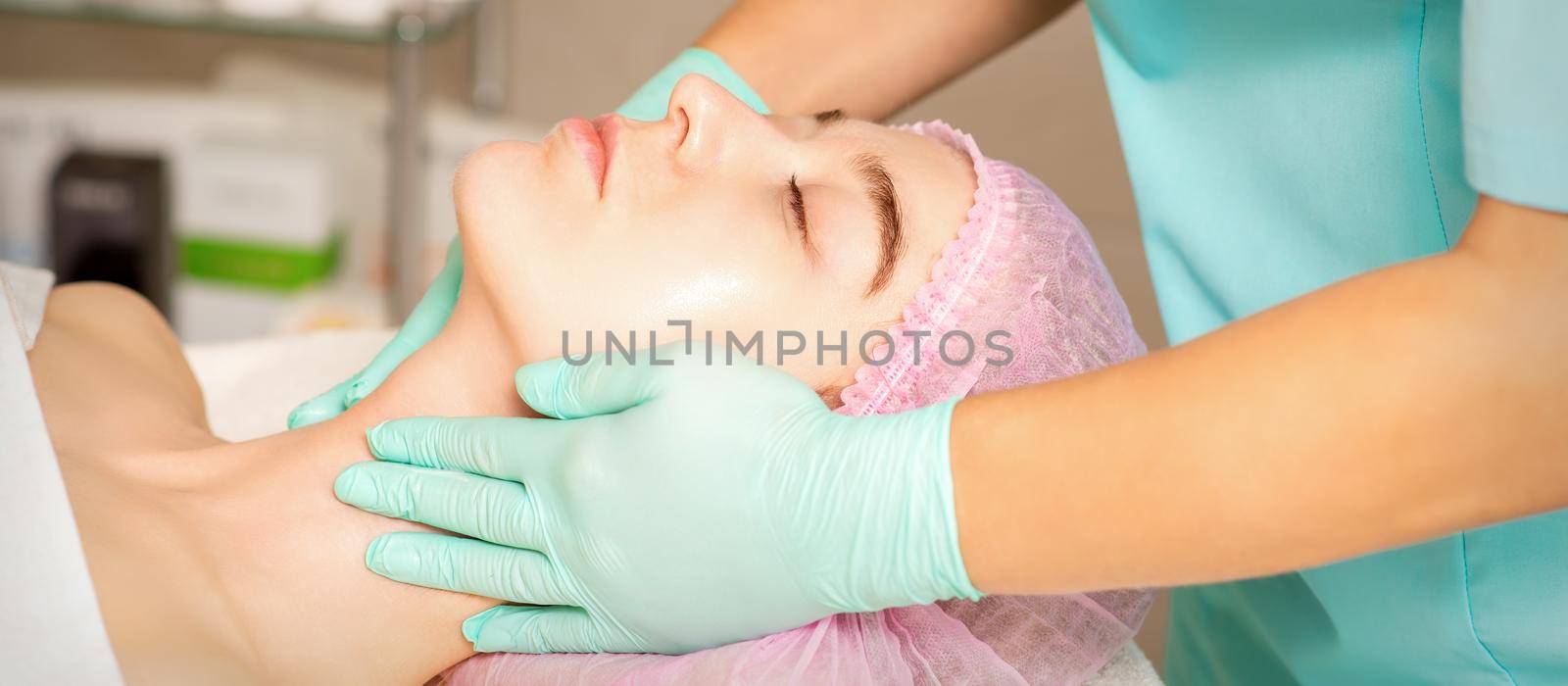 Cosmetologist with gloved hands applies a moisturizing mask with peeling cream on the female face. Facial cosmetology treatment. Procedures for facial care. by okskukuruza