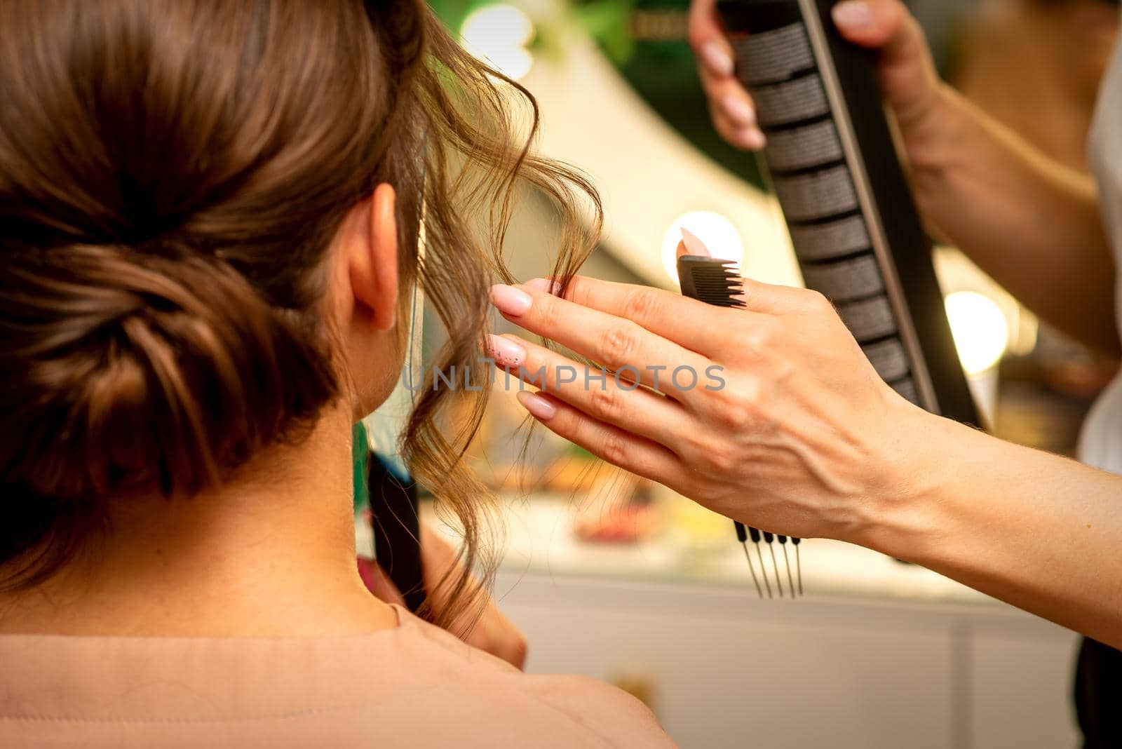 Professional hairdresser styling and fixing with hairspray long woman curly hair in a beauty salon. by okskukuruza