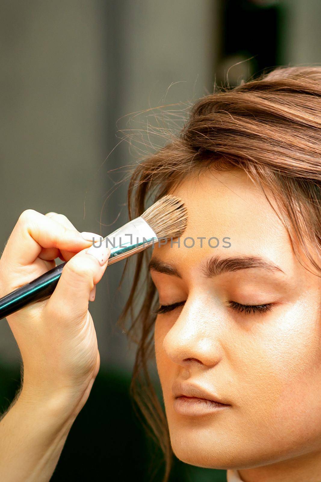 The makeup artist applies a cosmetic tonal foundation on the face using a makeup brush