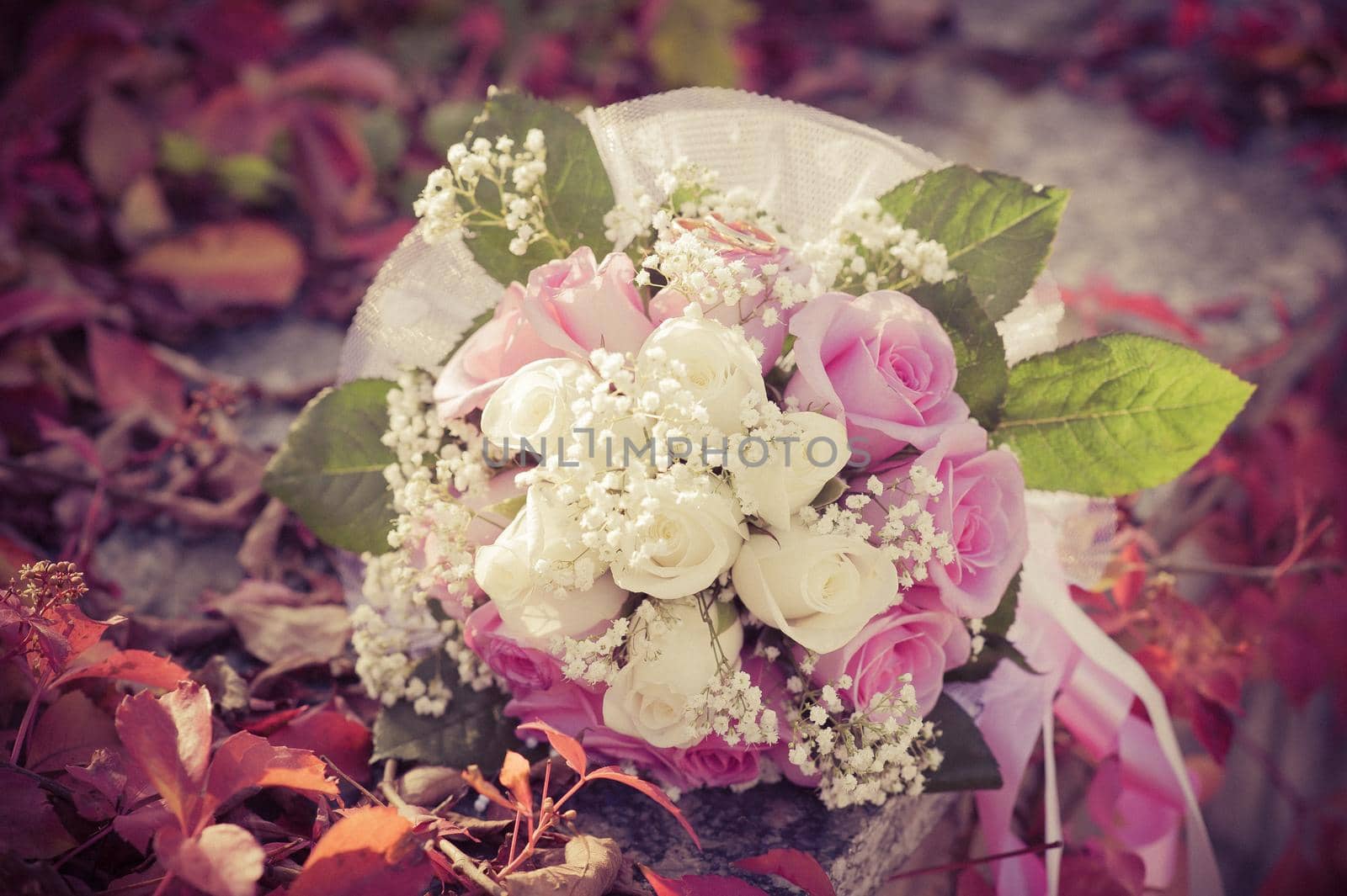 Bridal wedding bouquet of flowers with golden rings. Wedding bouquet of pink and white roses lying on a grass by Andrii_Ko