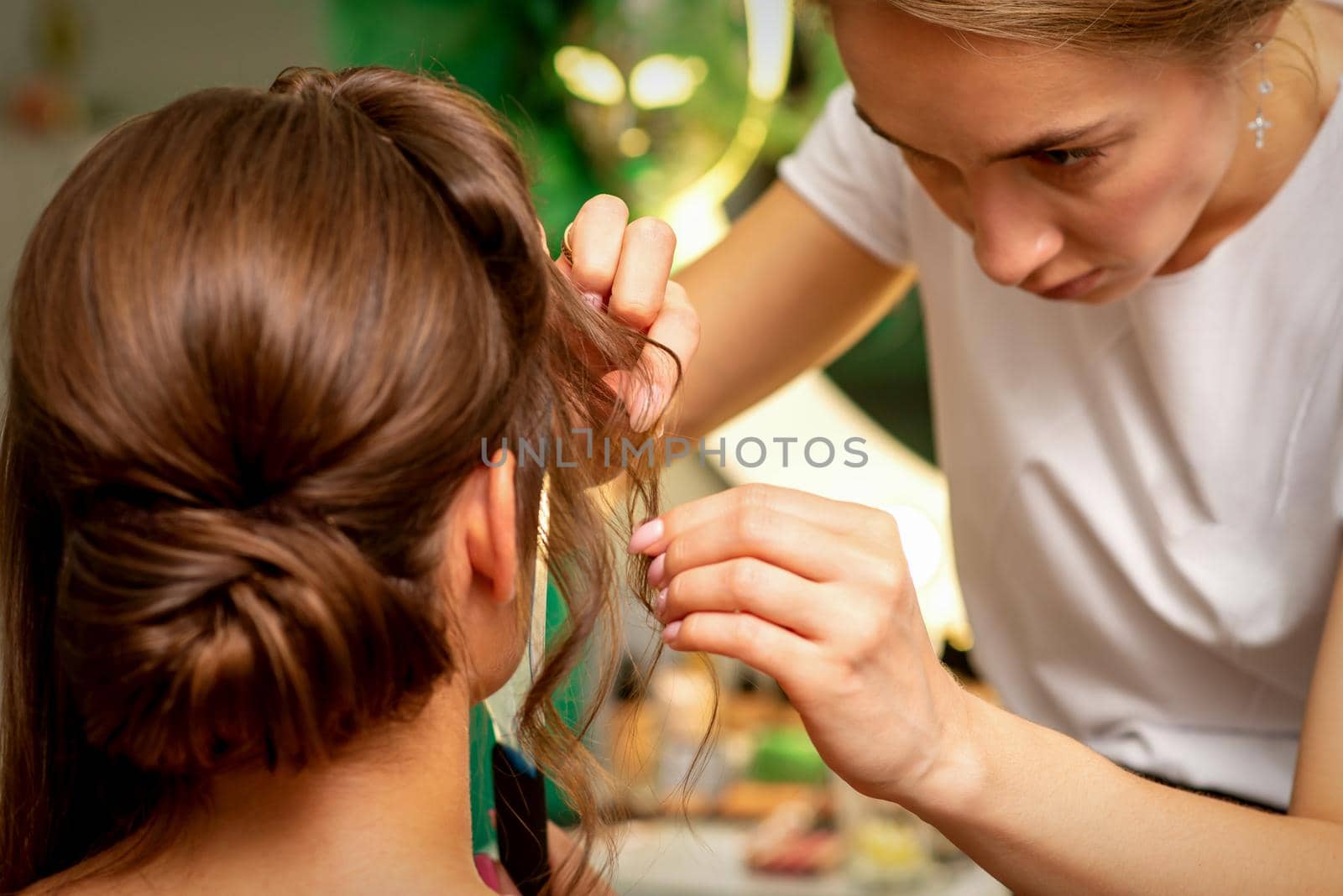 Hairstyling bride. A female hairdresser makes styling hair for the beautiful young caucasian woman in a beauty salon