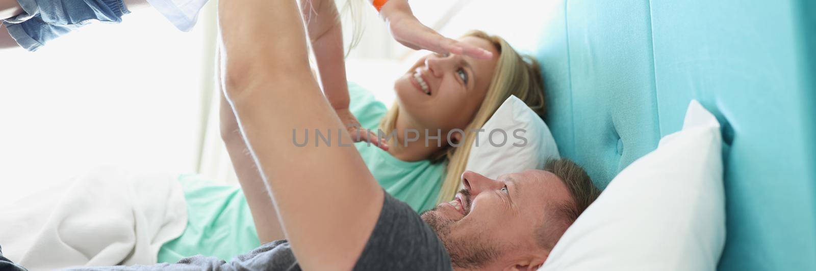 Lying on the bed, the parents lifted the child up, close-up, blurry. Mom and Dad in the hotel are happy with their daughter