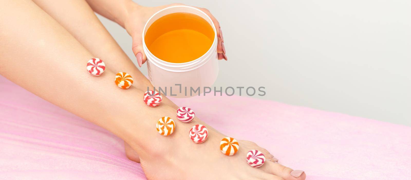 Depilation, waxing concept. Round candies lying down in a row on the female leg with a jar of sugar paste, close up. by okskukuruza