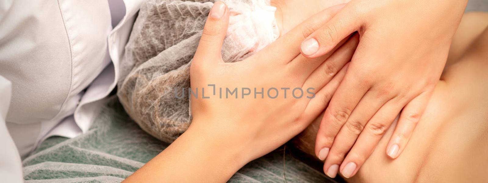 Facial massage. Hands of a masseur massaging neck of a young caucasian woman in a spa salon, the concept of health massage. by okskukuruza