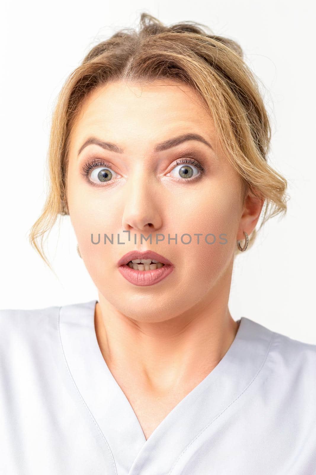 Female doctor shocked. Close up portrait of a young caucasian woman looking surprised with wide eyes stared isolated white wall background