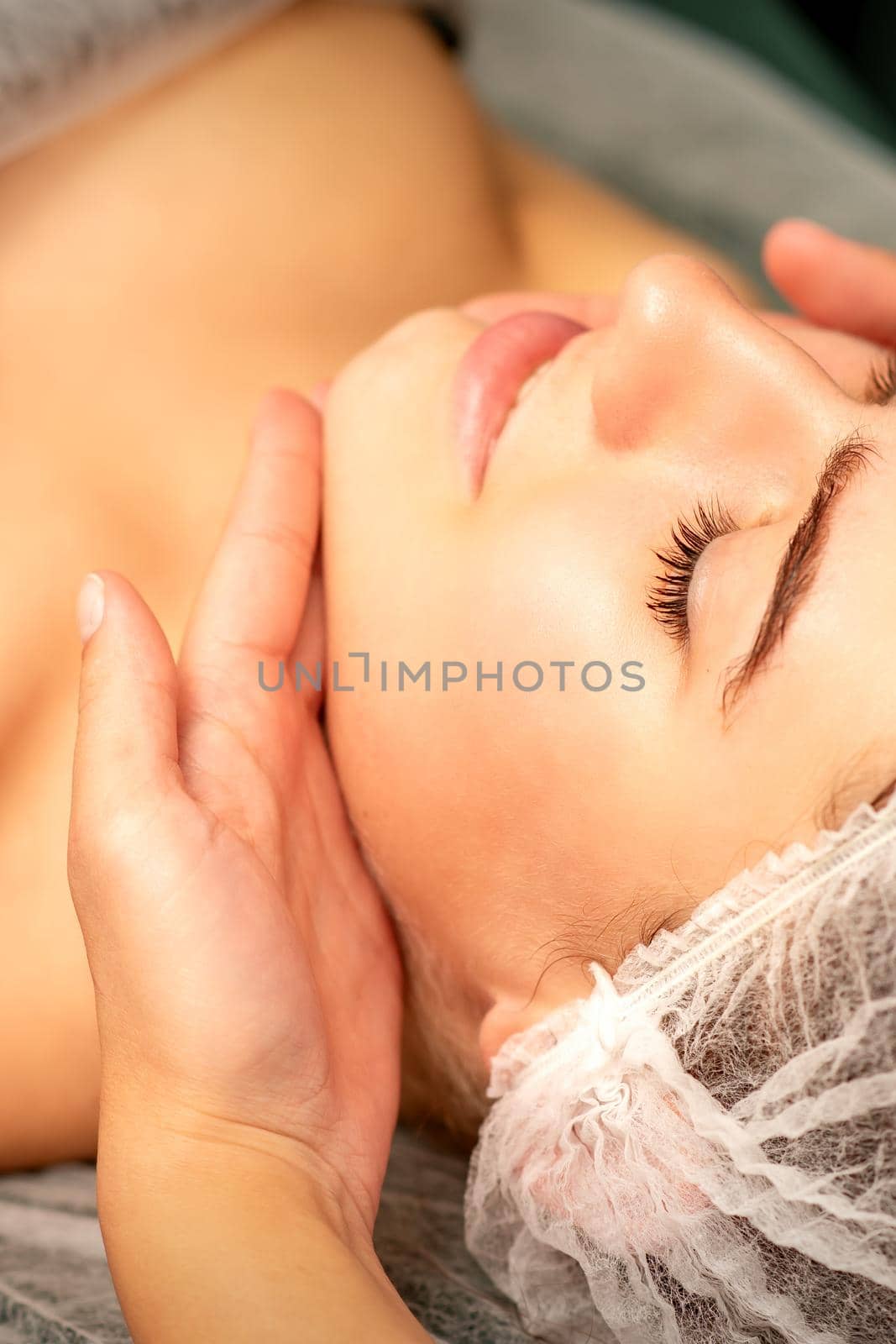 Facial massage. Hands of a masseur massaging neck of a young caucasian woman in a spa salon, the concept of health massage