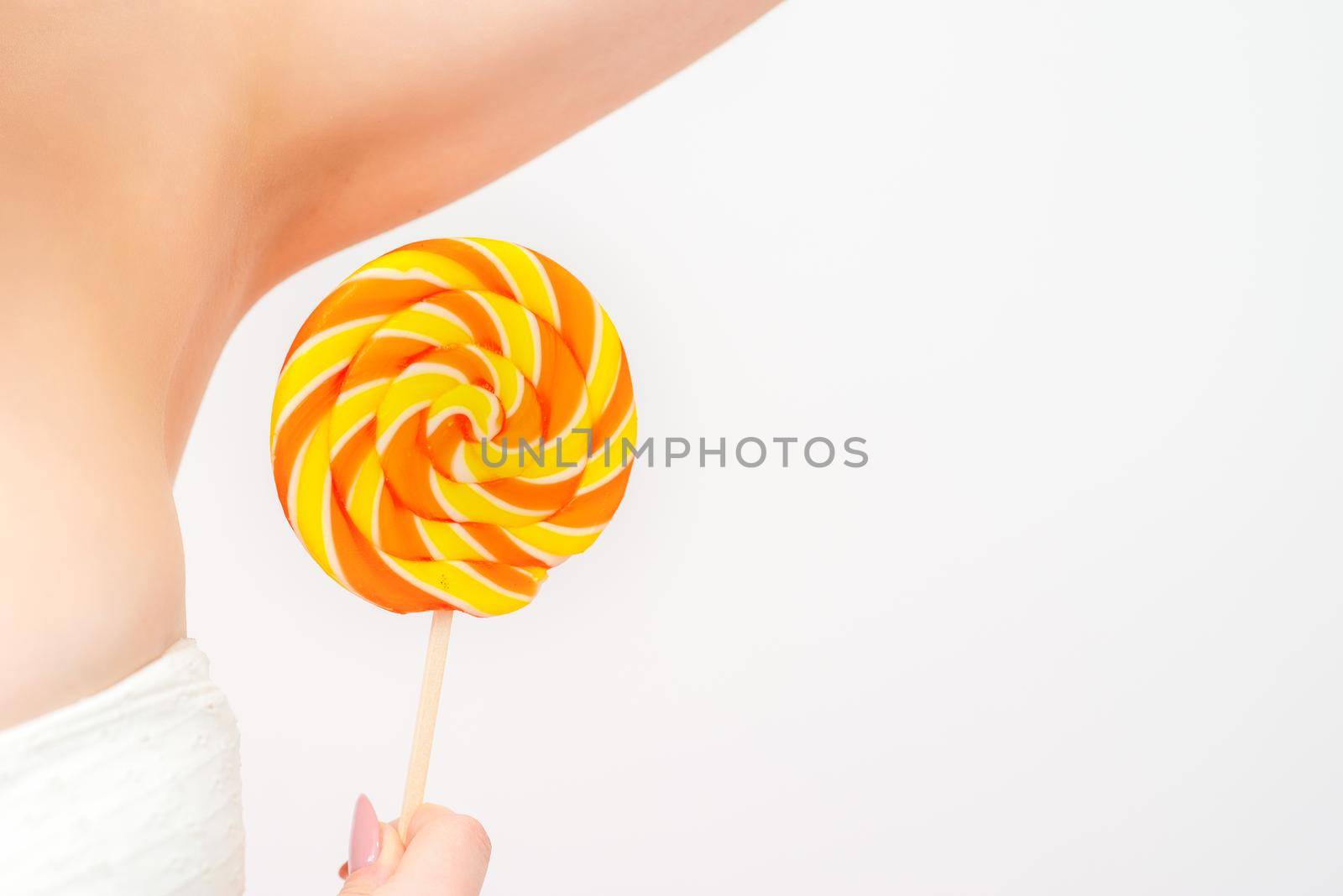 Waxing, depilation concept. A young female holds a round lollipop near her armpit on white background. by okskukuruza