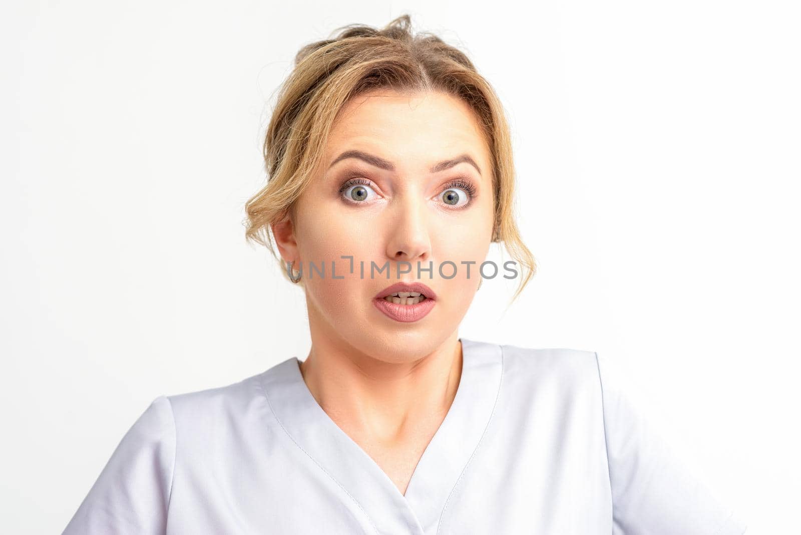 Female doctor shocked. Close up portrait of a young caucasian woman looking surprised with wide eyes stared isolated white wall background