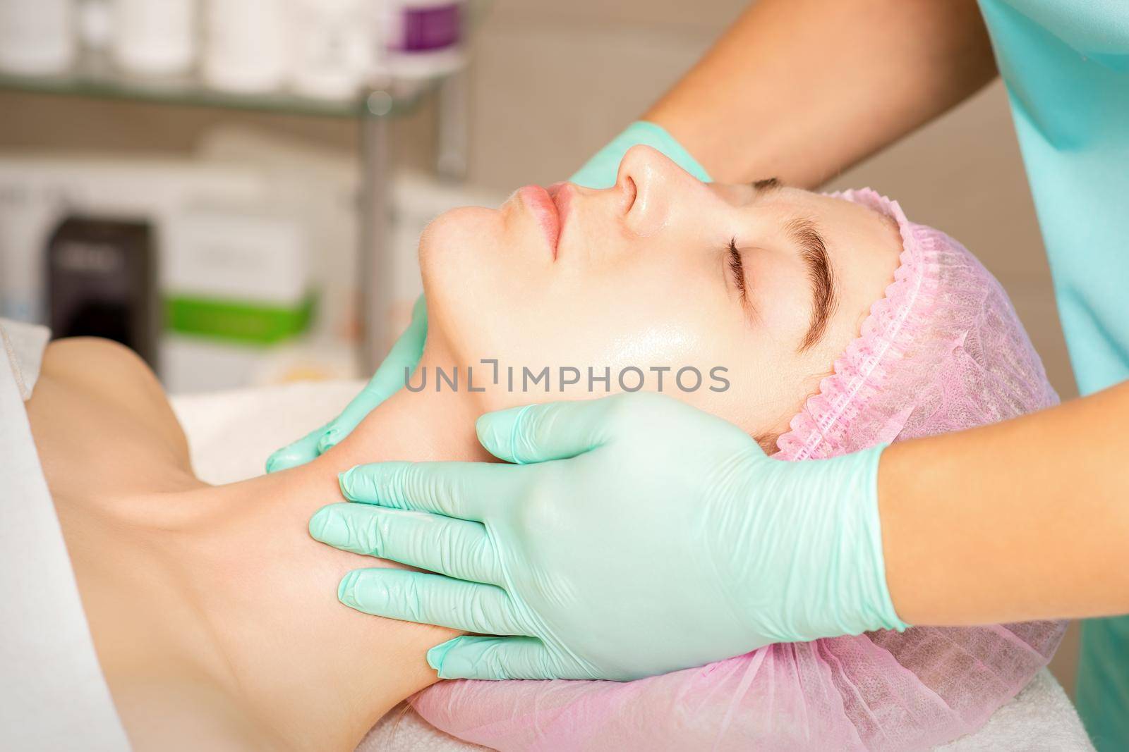 Cosmetologist with gloved hands applies a moisturizing mask with peeling cream on the female face. Facial cosmetology treatment. Procedures for facial care