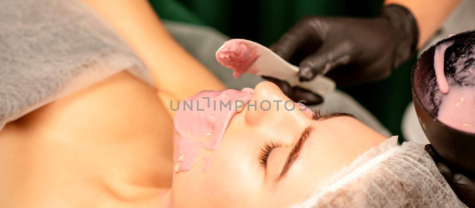 Beautiful young caucasian woman receiving an alginic mask to the face in beauty salon. Facial skin treatment. by okskukuruza