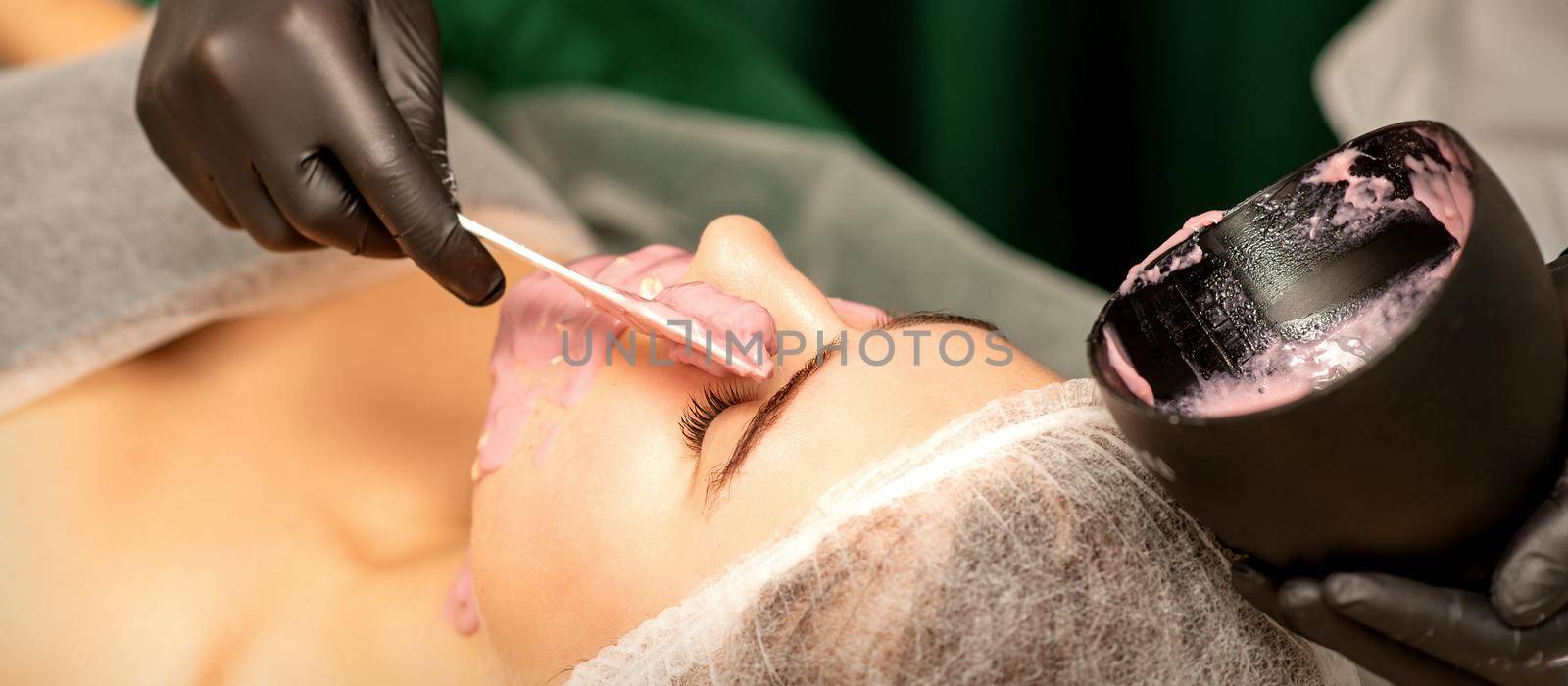 Beautiful young caucasian woman receiving an alginic mask to the face in beauty salon. Facial skin treatment