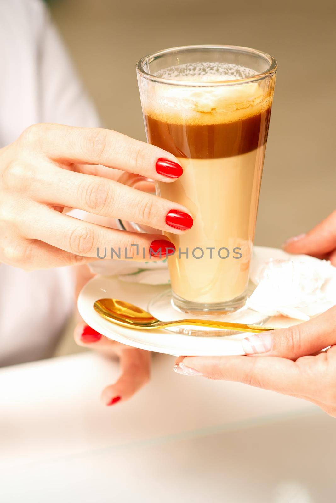 Barista serving coffee latte in glass mug for a customer, close up hands
