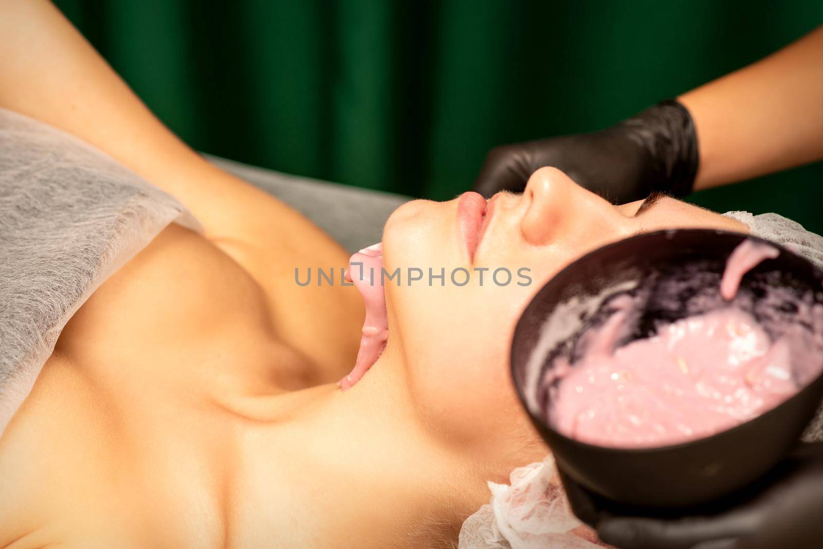 Beautiful young caucasian woman receiving an alginic mask to the face in beauty salon. Facial skin treatment