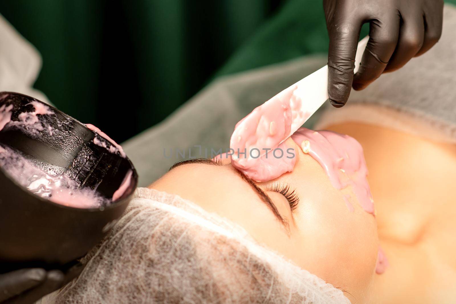 Beautiful young caucasian woman receiving an alginic mask to the face in beauty salon. Facial skin treatment