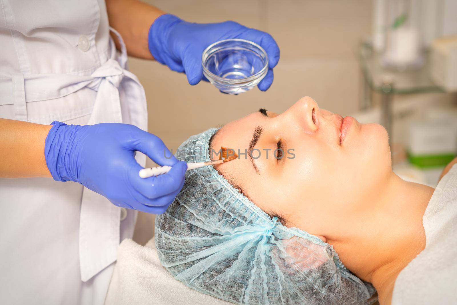 Young white woman getting acid organic retinol peel face skin with the brush in a beauty clinic. by okskukuruza