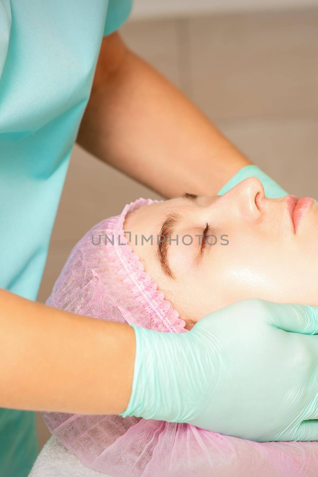 Cosmetologist with gloved hands applies a moisturizing mask with peeling cream on the female face. Facial cosmetology treatment. Procedures for facial care