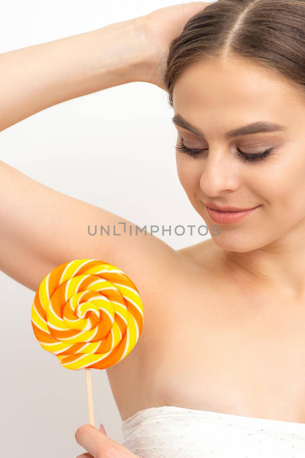 Waxing, depilation concept. The beautiful young caucasian woman covers her armpit with a lollipop on white background. by okskukuruza