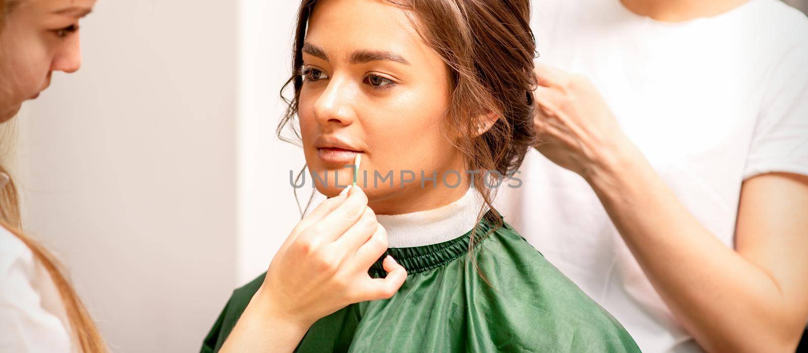 Makeup artist and hairdresser prepare the bride making hairstyle and makeup in a beauty salon. by okskukuruza