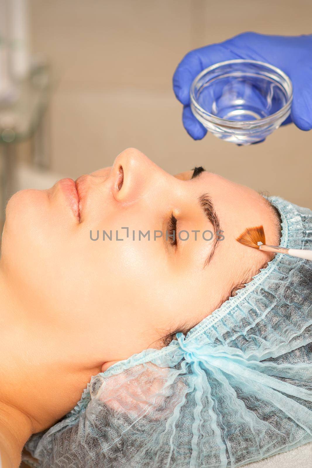 Young white woman getting acid organic retinol peel face skin with the brush in a beauty clinic