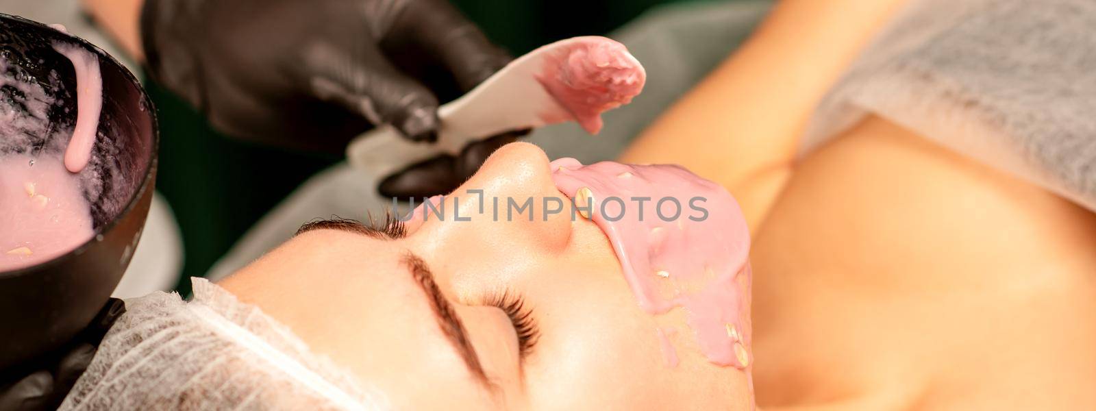 Beautiful young caucasian woman receiving an alginic mask to the face in beauty salon. Facial skin treatment. by okskukuruza