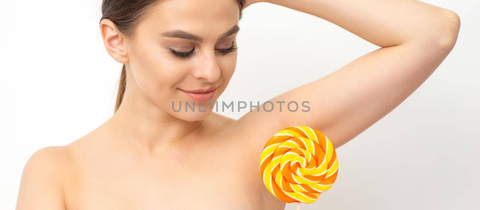 Waxing, depilation concept. The beautiful young caucasian woman covers her armpit with a lollipop on white background