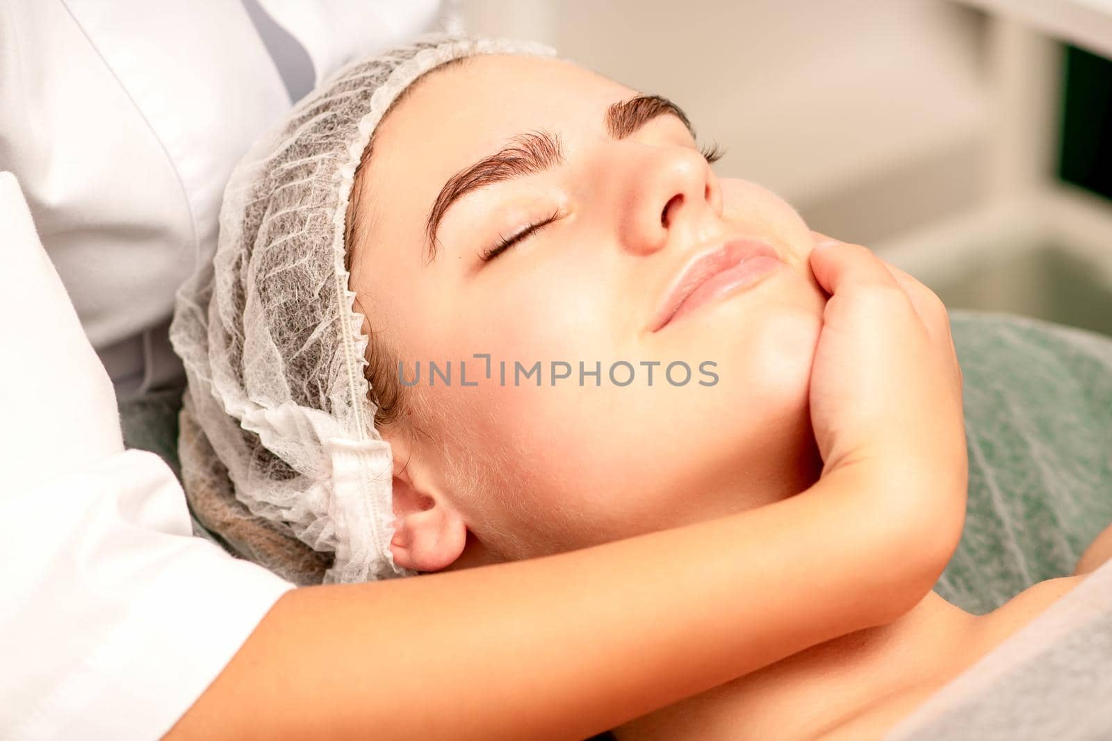 Facial massage. Hands of a masseur massaging neck of a young caucasian woman in a spa salon, the concept of health massage. by okskukuruza