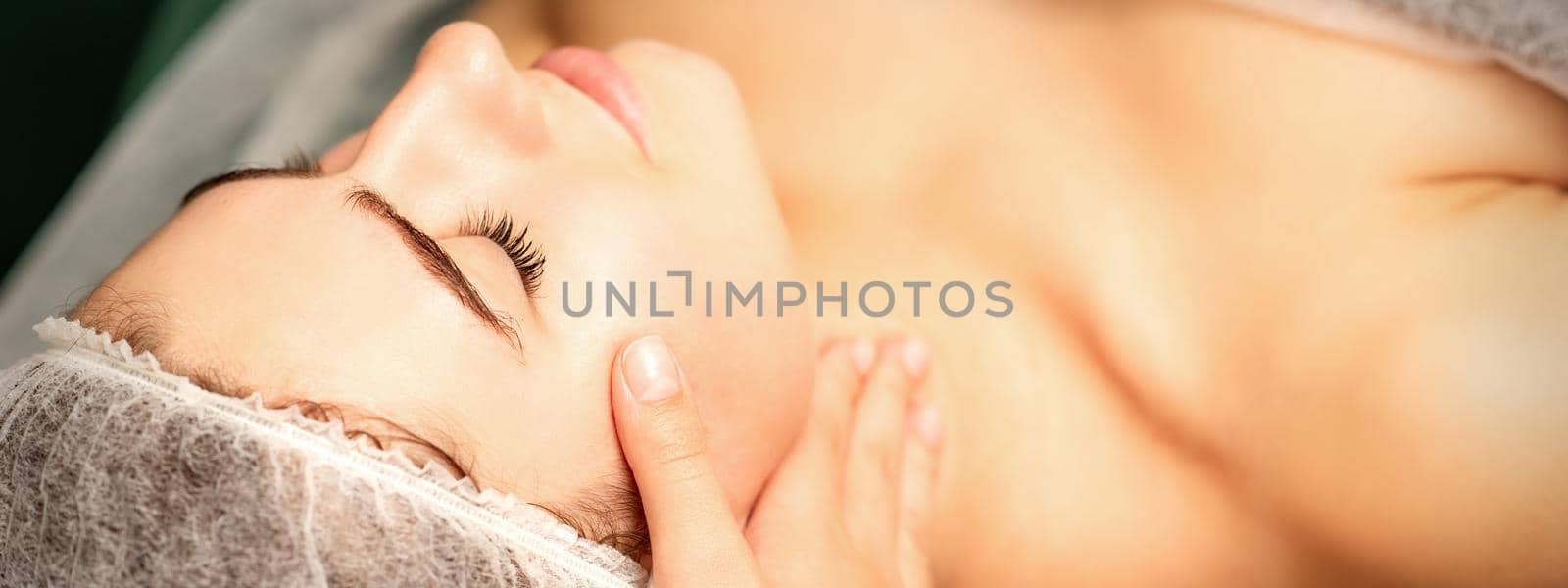 Facial massage. Hands of a masseur massaging neck of a young caucasian woman in a spa salon, the concept of health massage. by okskukuruza