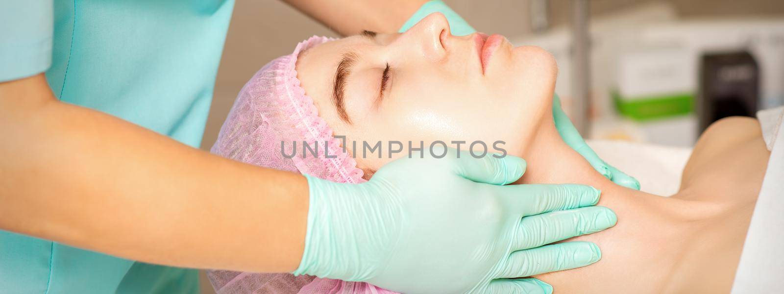 Cosmetologist with gloved hands applies a moisturizing mask with peeling cream on the female face. Facial cosmetology treatment. Procedures for facial care. by okskukuruza