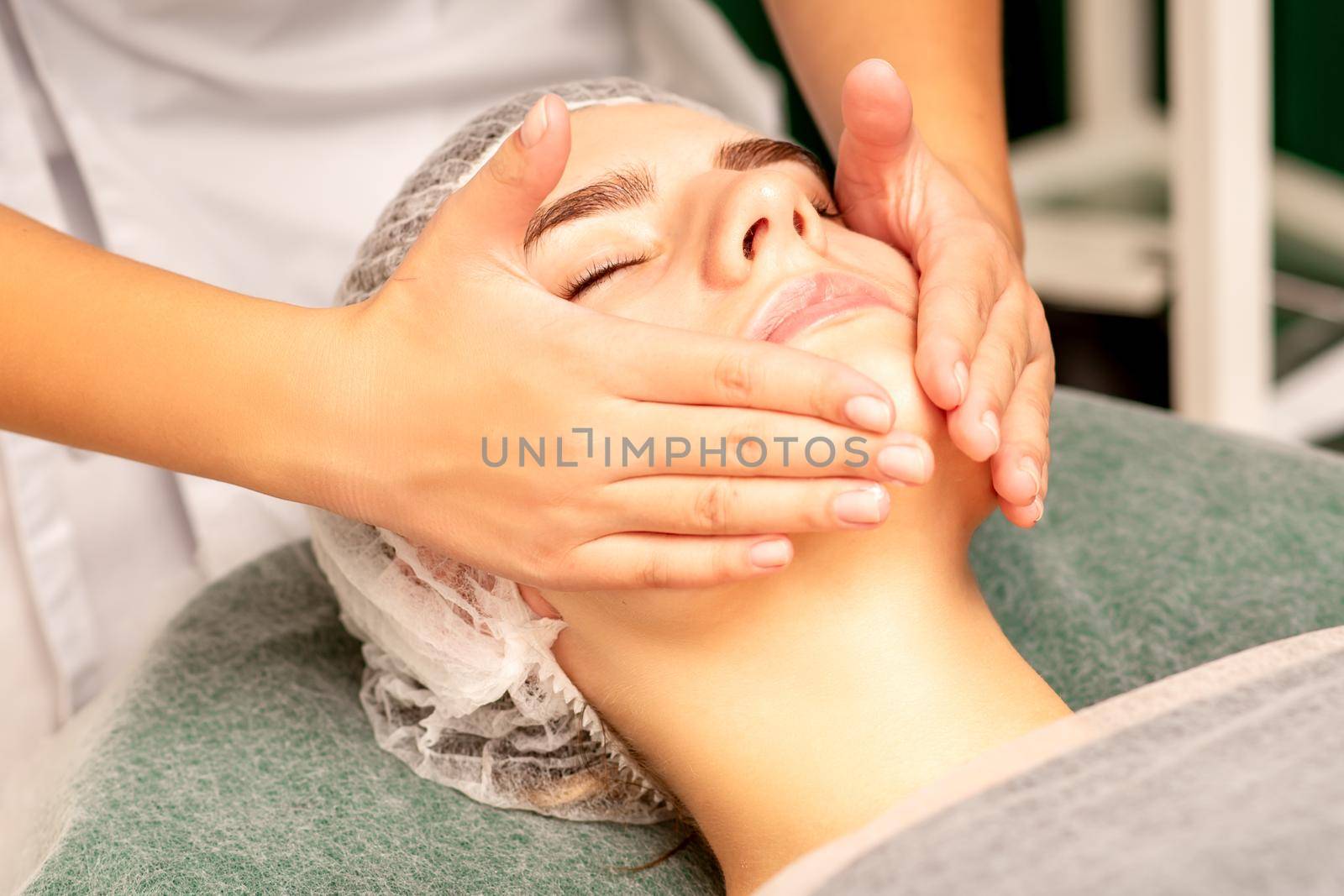 Facial treatment massage. Beautiful young caucasian woman with perfect skin receiving face and neck massage at a beauty spa