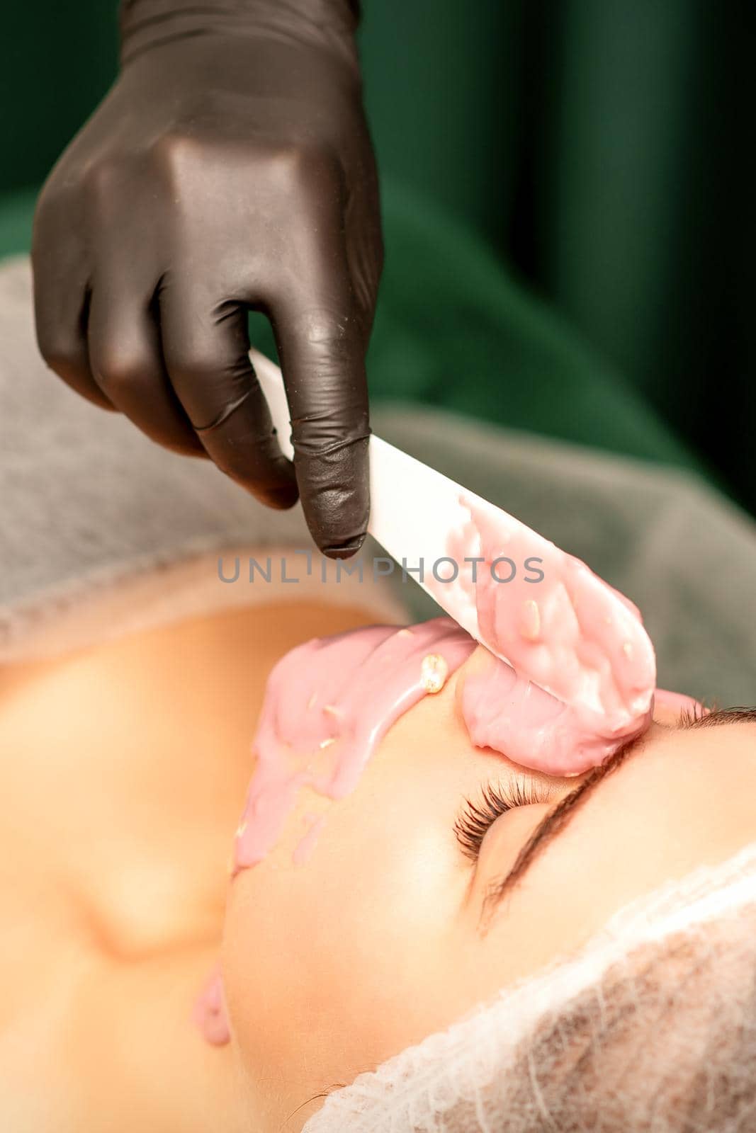 Beautiful young caucasian woman receiving an alginic mask to the face in beauty salon. Facial skin treatment. by okskukuruza