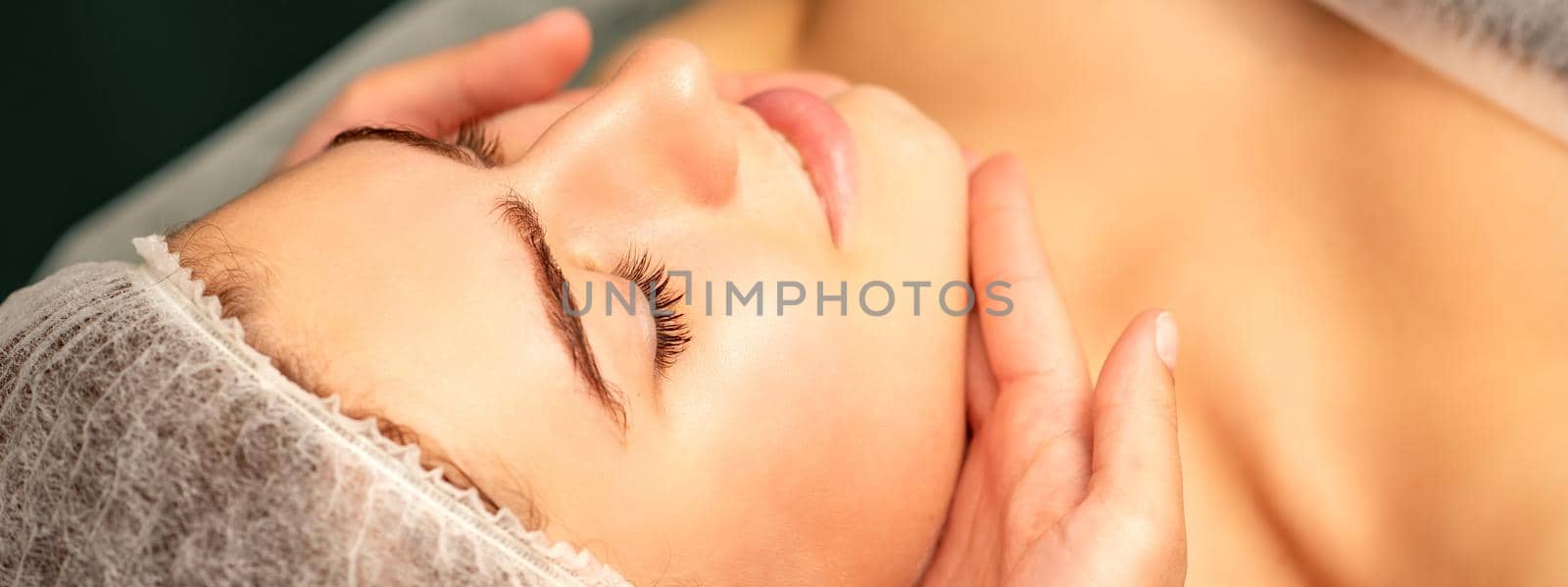 Facial massage. Hands of a masseur massaging neck of a young caucasian woman in a spa salon, the concept of health massage