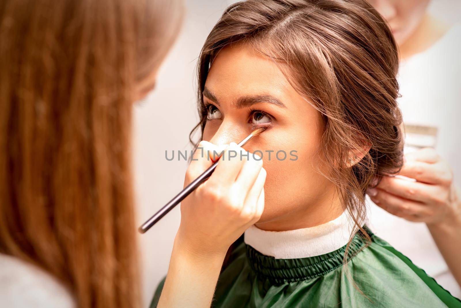 Makeup artist and hairdresser prepare the bride making hairstyle and makeup in a beauty salon