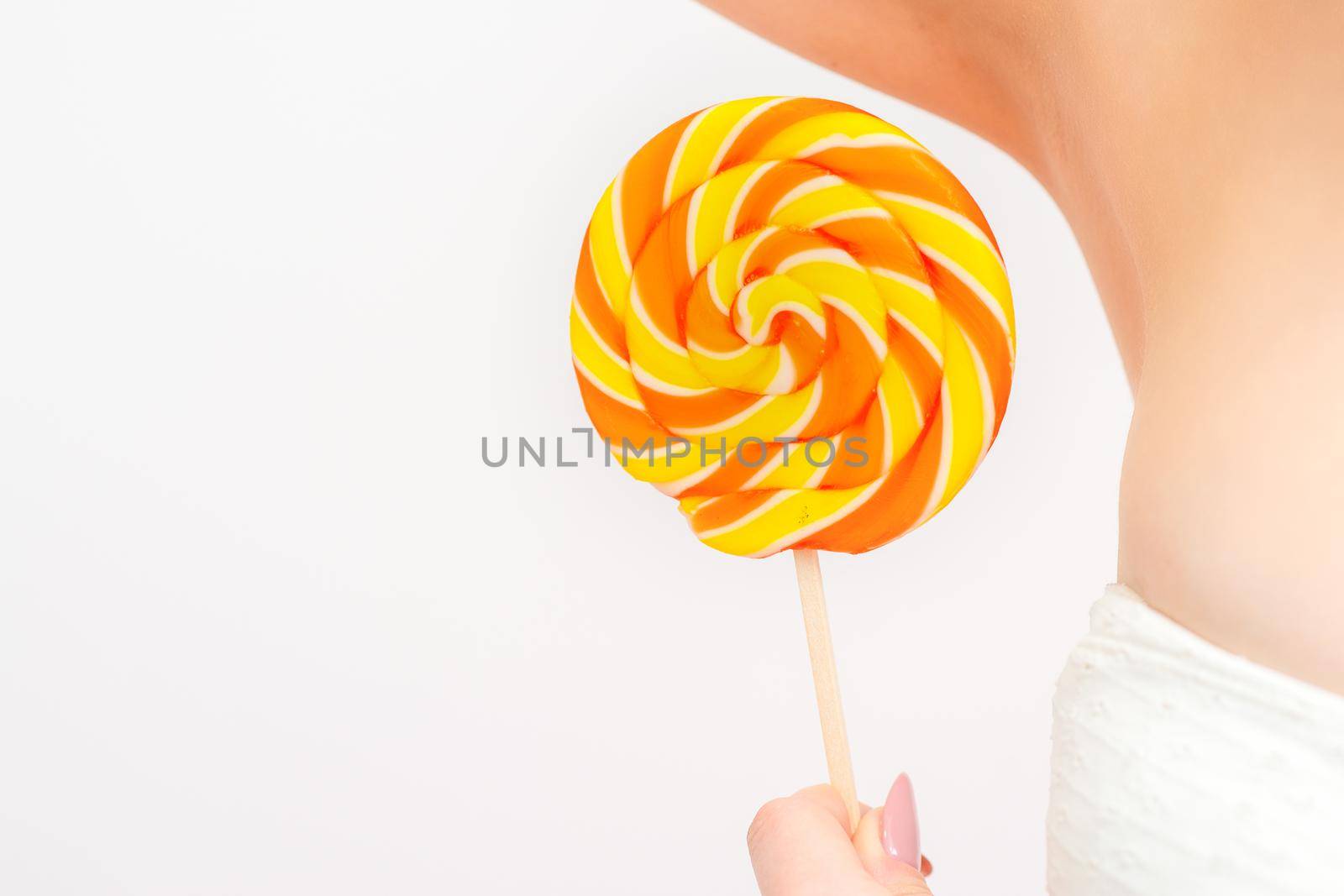 Waxing, depilation concept. A young female holds a round lollipop near her armpit on white background