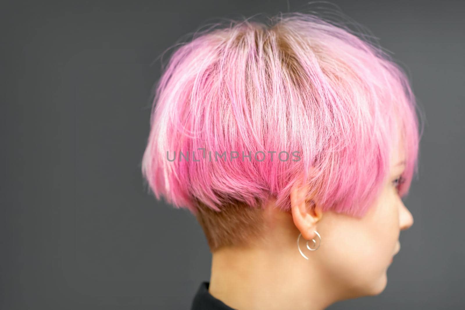 Profile of a beautiful young caucasian woman with short bob pink hairstyle on dark gray background