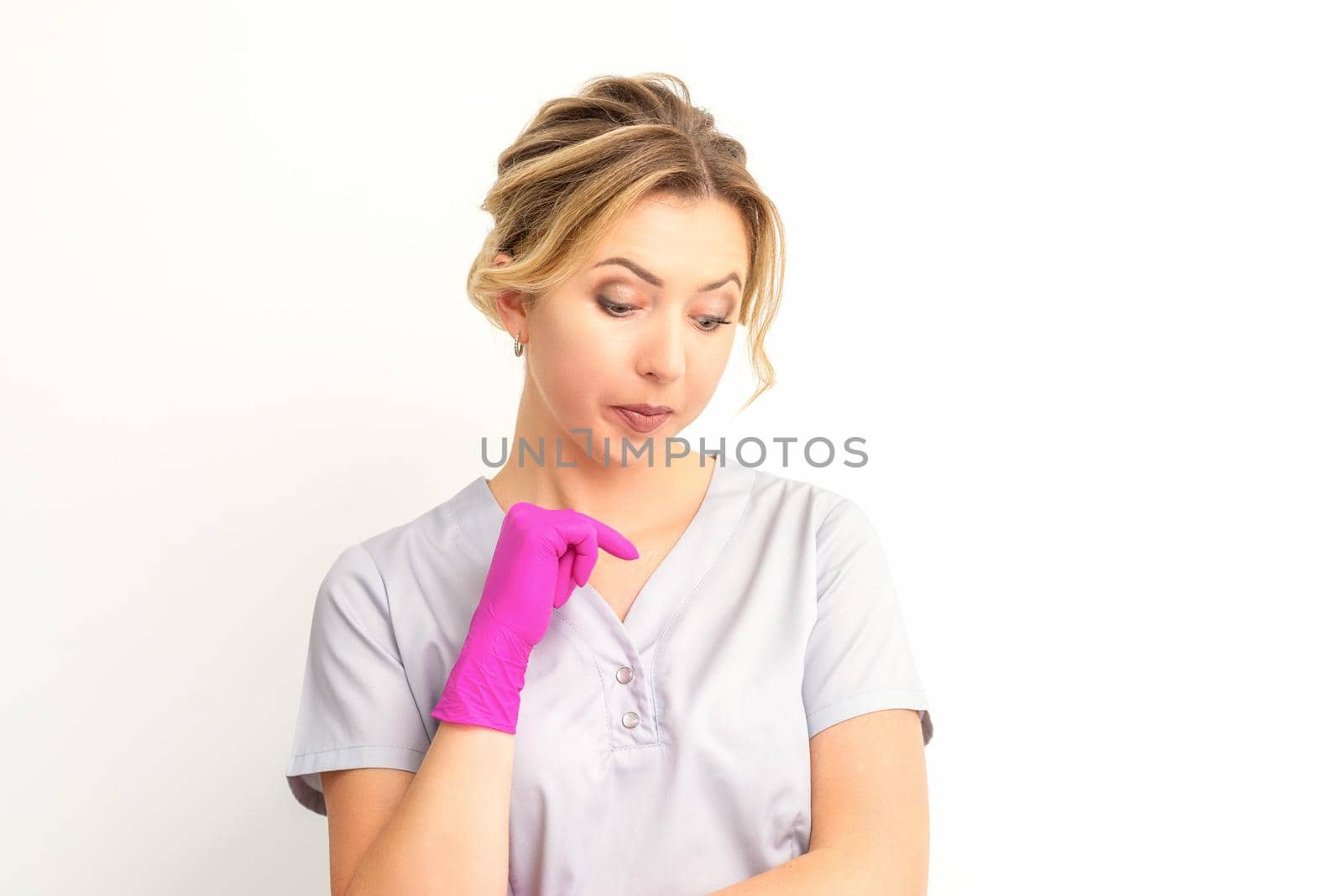 Young caucasian female doctor wearing gloves thoughtful looking down against a white background