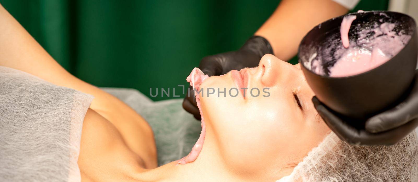 Beautiful young caucasian woman receiving an alginic mask to the face in beauty salon. Facial skin treatment. by okskukuruza