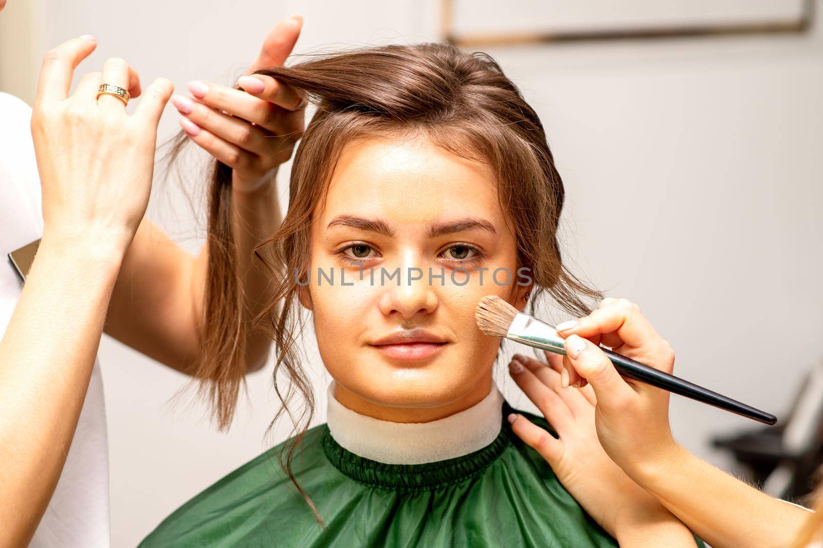 Makeup artist and hairdresser prepare the bride making hairstyle and makeup in a beauty salon. by okskukuruza