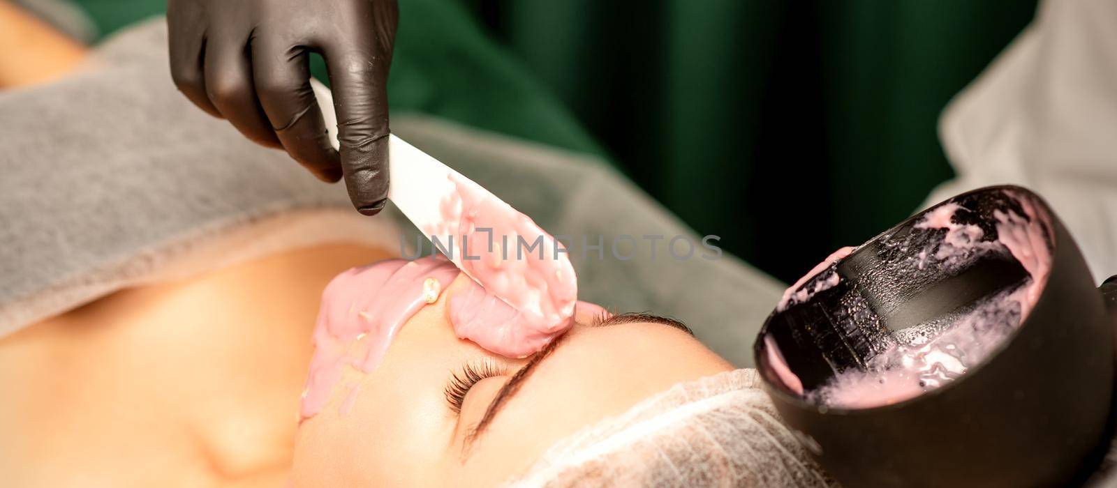 Beautiful young caucasian woman receiving an alginic mask to the face in beauty salon. Facial skin treatment. by okskukuruza