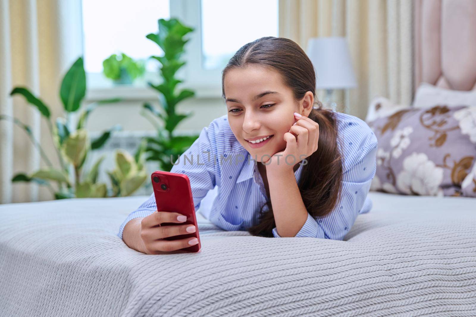 Young teenage female lying at home with smartphone, girl resting on bed using mobile apps. Lifestyle, technology, leisure, adolescence concept