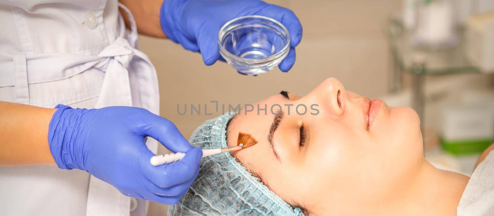 Young white woman getting acid organic retinol peel face skin with the brush in a beauty clinic