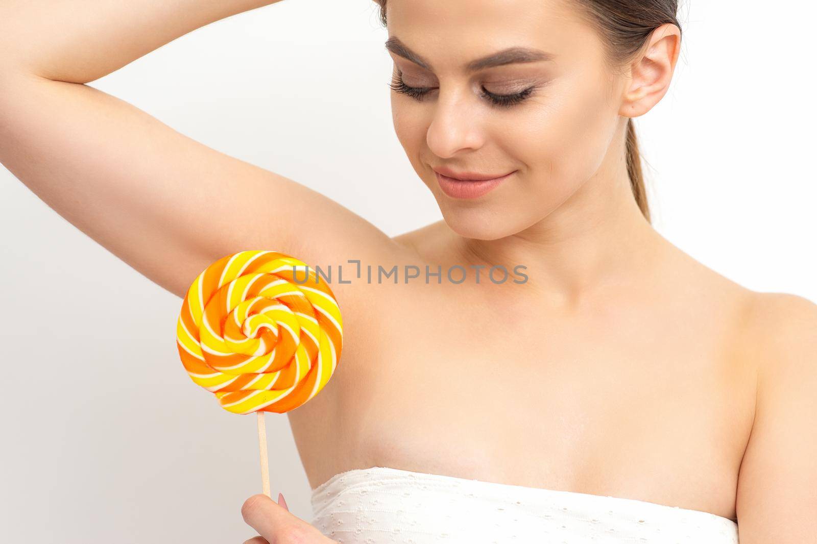 Waxing, depilation concept. The beautiful young caucasian woman covers her armpit with a lollipop on white background. by okskukuruza