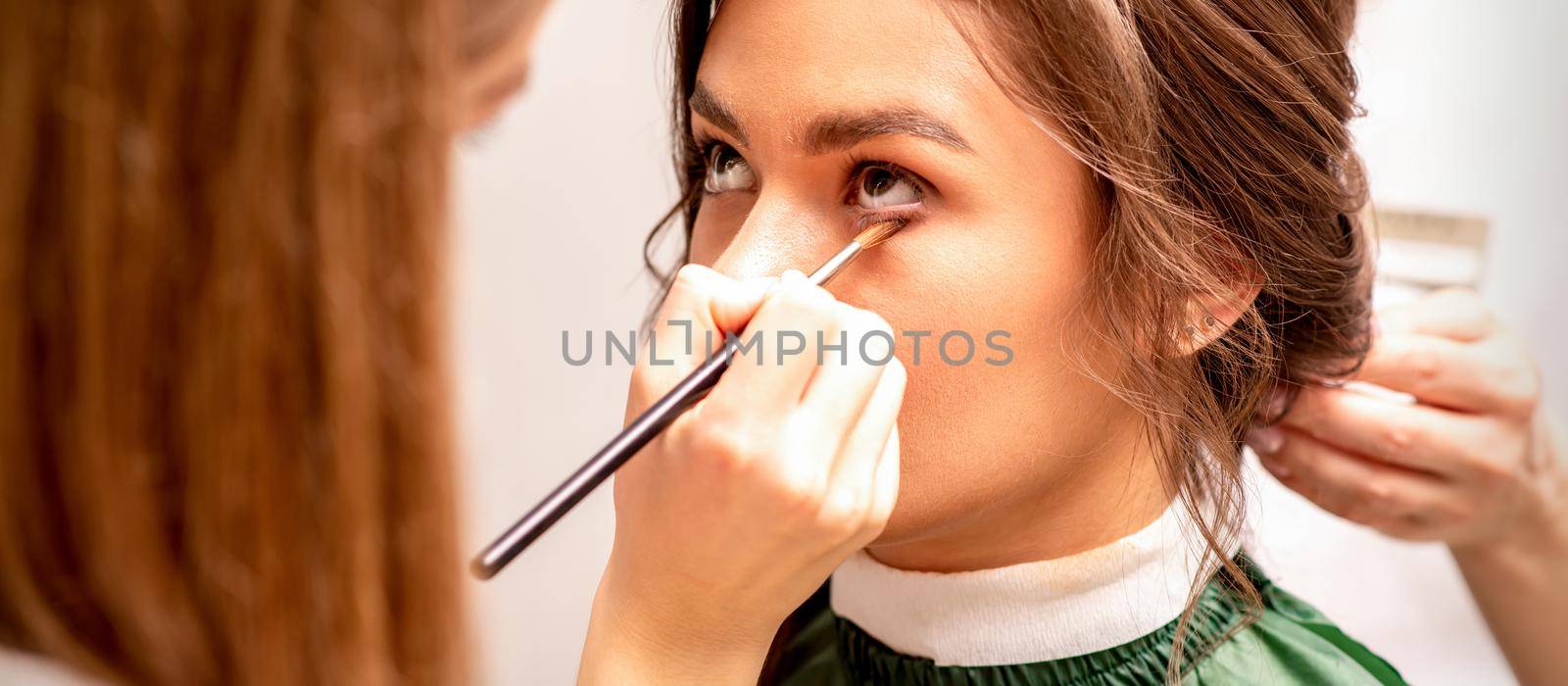 Makeup artist and hairdresser prepare the bride making hairstyle and makeup in a beauty salon. by okskukuruza